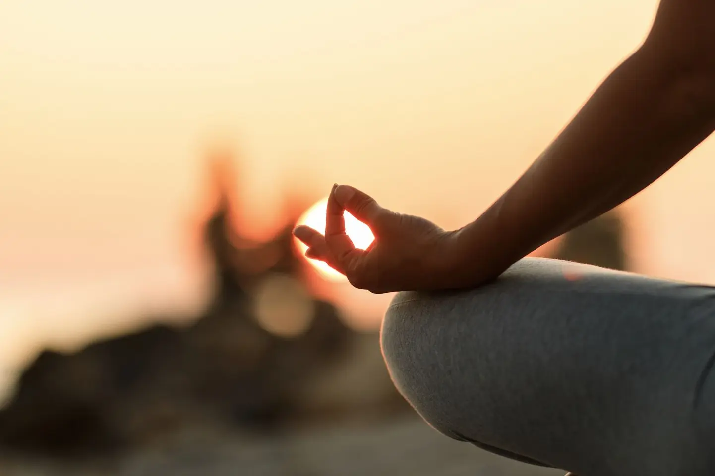 Meditation im Sonnenuntergang "Nahaufnahme einer Person in Meditationshaltung am Strand bei Sonnenuntergang. Die Hand formt ein Mudra, während die Sonne im Hintergrund scheint."