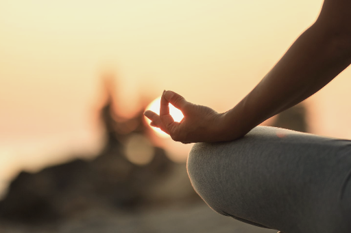Meditation im Sonnenuntergang "Nahaufnahme einer Person in Meditationshaltung am Strand bei Sonnenuntergang. Die Hand formt ein Mudra, während die Sonne im Hintergrund scheint."